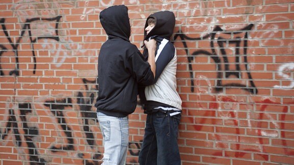 Ein Teenager drückt einen kleineren gewaltsam gegen eine Wand, gestellte Szene