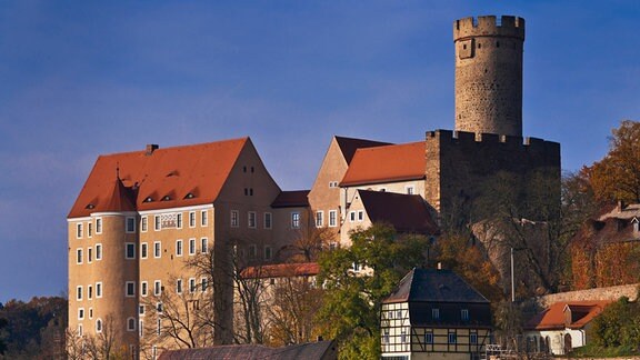 Burg Gnandstein, mehrere Gebäude und ein Turm mt Zinnen, vor blauem Himmel