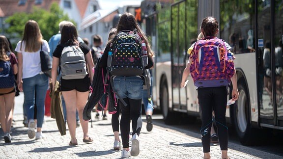 Schülerinnen gehen an einer Bushaltestelle zu wartenden Bussen