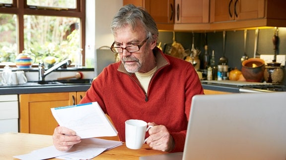Ein Mann sitzt mit aschenrechner über einem Schreiben. - Symbolbild