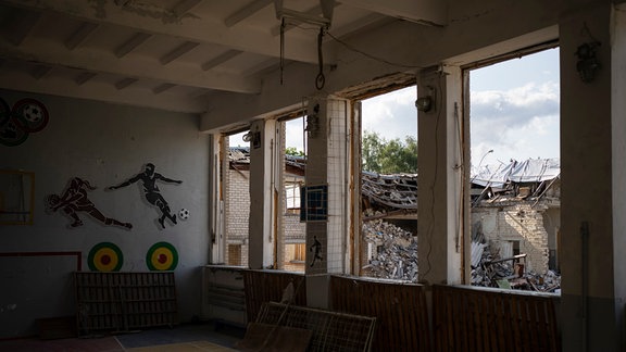 Die zerstörte Bibliothek einer Schule ist durch die zerbrochenen Fenster einer Turnhalle zu sehen.
