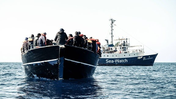 Menschen sitzen bei einer Rettungsaktion von der Hilfsorganisation Sea-Watch auf einem Boot.