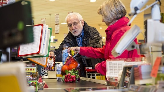 Senioren legen im Supermarkt an der Kasse ihre Ware auf das Band