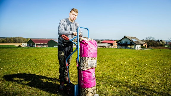 Landwirt Andreas Fritsch (24), Co-Betriebsleiter "Petra Fritsch Landwirtschaft", steht mit zwei Säcken Soja-Saatgut auf einer Wiese vor seinem Hof. 