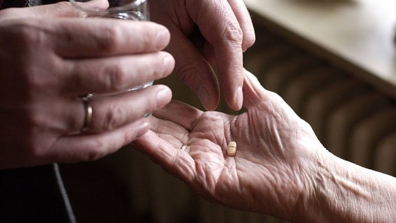 Eine Tablette wird in die Hand einer Seniorin gelegen