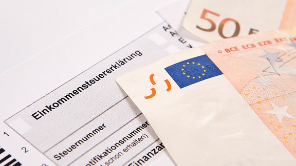 Das Formular der Einkommensteuererklärung und zwei 50-Euro-Scheine liegen auf einem Tisch