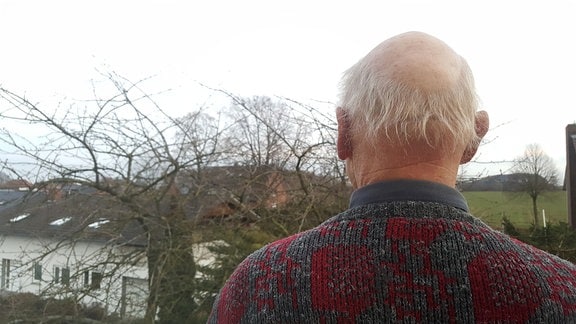 Ein älterer Mann von hinten. Er schaut in die Landschaft.
