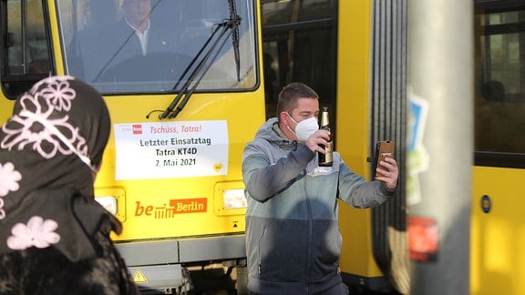 Ein Straßenbahn-Fan posiert mit einer Bierflasche in der Hand für ein Selfie vor einer Tatra-Straßenbahn in Berlin mit der Aufschrift "Tschüss, Tatra!"