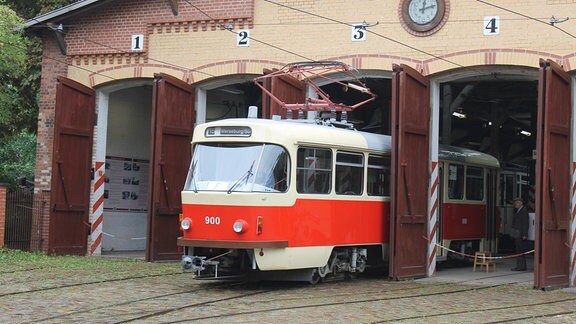 Eine rot-beige lackierte Tatra-Straßenbahn T4D mit Ausstiegstüren auf der linken und rechten Fahrseite fährt aus einem großen Holztor eines Depots heraus