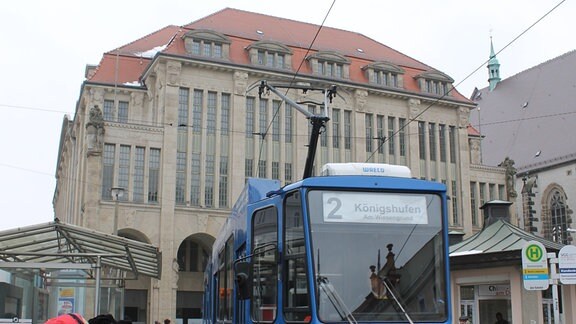 Ein blauer Tatra-Straßenbahn-Triebwagen der Linie 2 steht in Görlitz vor dem historischen Warenhaus an einer Haltestelle