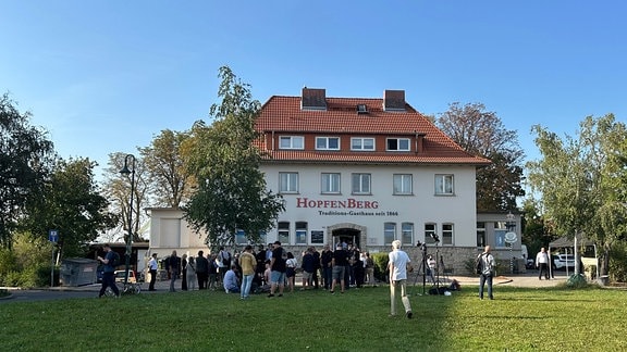 Vor einem Haus mit dem Namen "Hopfenberg" steht eine Menschengruppe.