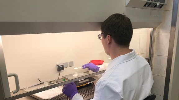 Ein Mann in weißer Schutzkleidung arbeitet in einem Labor.