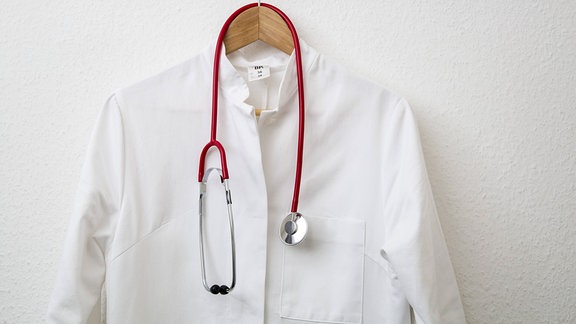 Ein Arztkittel hängt am Bügel, am Garderobenhaken, mit Stethoskop. 