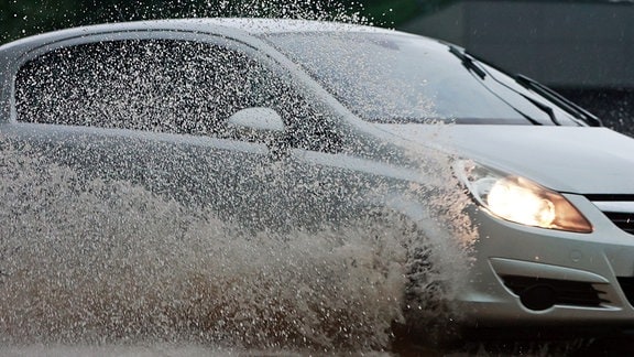 Ein Auto fährt nach einem Unwetter mit Starkregen über eine überflutete Straße.