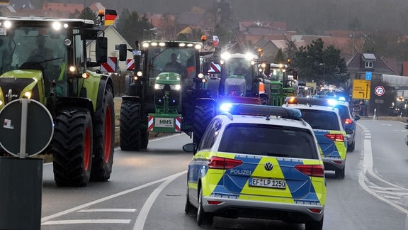 Polizeifahrzeuge begleiten Landwirte, die mit ihren Traktoren über die Bundesstraße 7 fahren. 