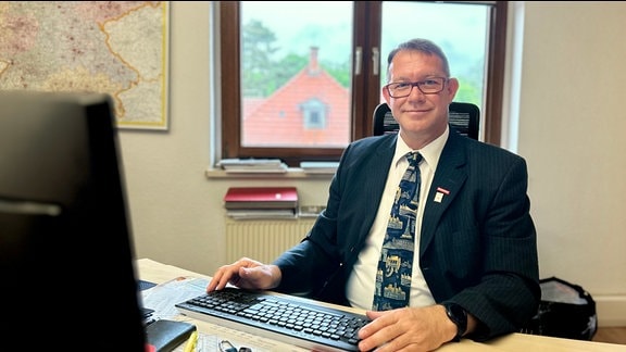 Bestatter Ronald Häring sitzt in seinem Büro am Schreibtisch. Im Hintergrund ist ein Fenster.
