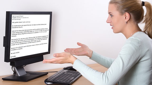 Frau schaut ratlos auf den Monitor, auf welchen sich eine E-Mail mit einer Zahlungsaufforderung befindet.