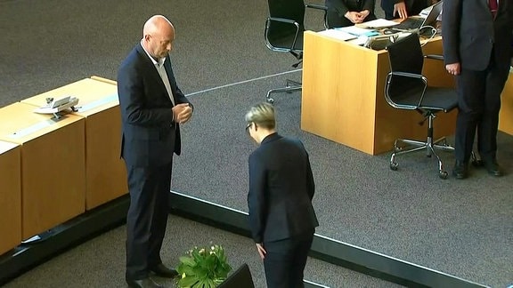 Die Linke-Fraktionschefin Susanne Hennig-Wellsow steht vor Ministerpräsident Thomas Kemmerich (FDP) im Thüringer Landtag. Zwischen beiden liegt ein Blumenstrauß auf dem Boden.