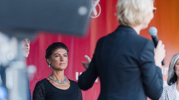 Sahra Wagenknecht hinten links auf einer Bühne, davor steht Katja Wolf.