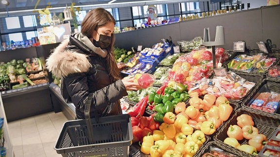 Eine Kundin mit Maske an der Gemüsetheke in einem Supermarkt.