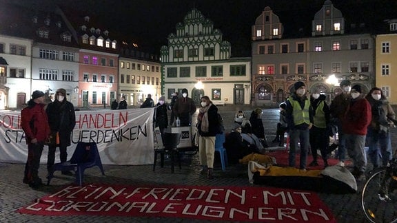 Menschen stehen im Dunkeln auf dem Marktplatz in Weimar und haben Transparente vor sich liegen.