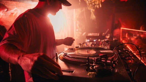 Symbolfoto: DJ am Plattenspieler in rotem Licht einer Diskothek