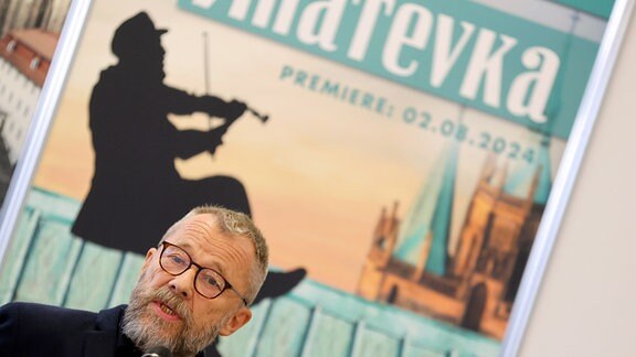 Der Regisseur der Domstufenfestspiele 2024, Ulrich Wiggers, sitzt vor einem Anatevka-Plakat bei der Presekonferenz zu den Domstufenfestspielen.