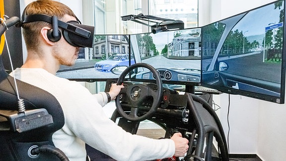 Ein junger Mann sitzt mit einer VR (Virtual Reality) Brille in einem 360 Grad Fahrsimulator.