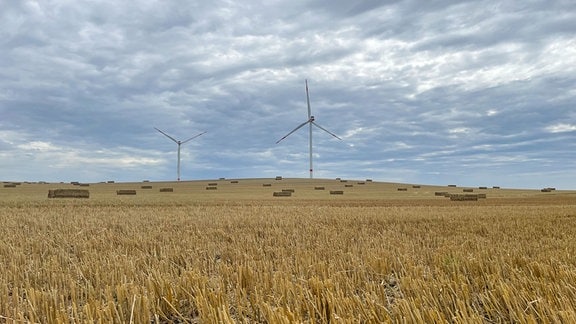 Zwei Windräder auf einem Feld auf dem Strohballen liegen.