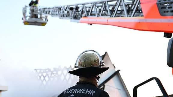 Ein Feuerwehrmann steht bei einem Einsatz bei einem Brand an einer Drehleiter.