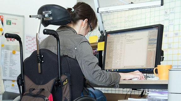  Eine Frau im Rollstuhl sitzt 2015 an einem Schreibtisch.