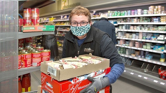 Eine Frau mit Mundschutz räumt in einem Supermarkt Regale ein