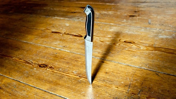 Ein Messer steckt in einem Holzfußboden.