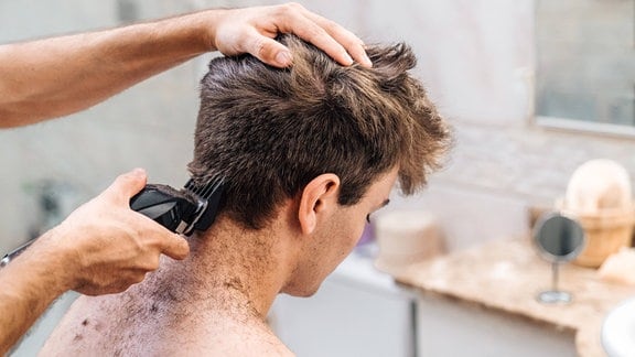 Einen jungen Mann werden die Haare geschnitten