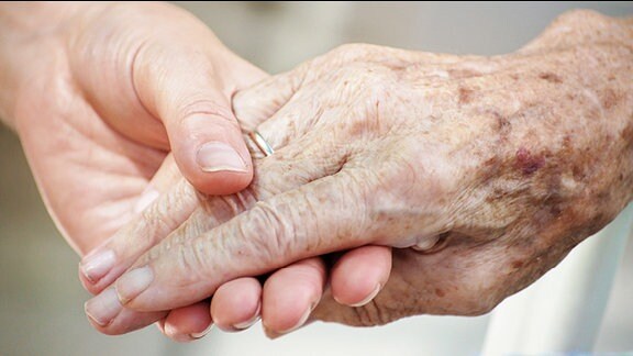 Eine Frau hält die Hand einer Seniorin.
