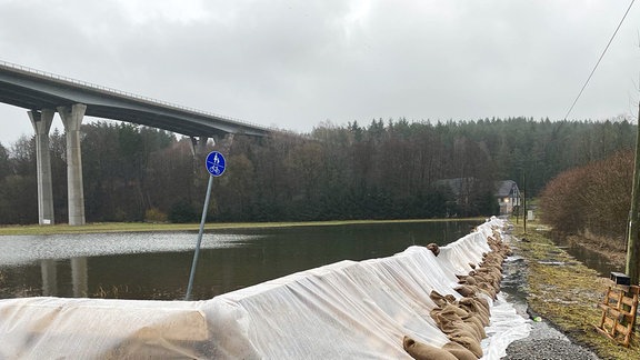 Sandsäcke schützen einen Damm, im Hintergrund eine Brücke.