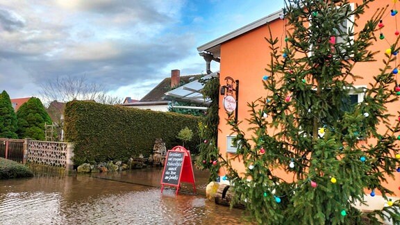 Einfahrt zu einer Gaststätte, die von Wasser überflutet ist, rechts im Bild ein Weihnachtsbaum