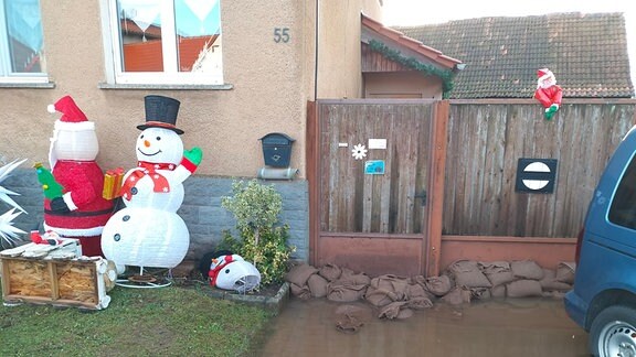 Eine Grundtückeinfahrt, die voller Wasser steht, daneben ein Plastikweihnachtsmann und ein Plastikschneemann.