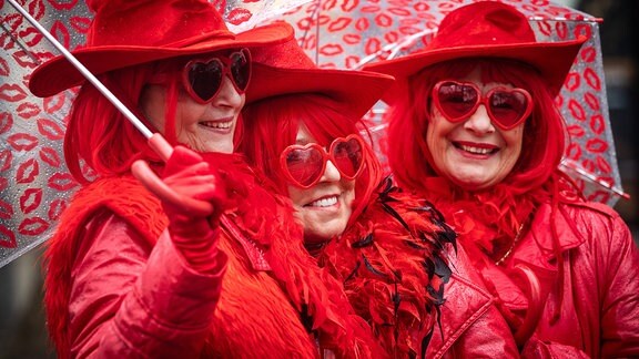 Drei Frauen mit roten Hüten und roten Sonnenbrillen feiern Karneval.