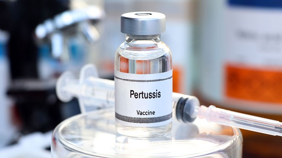 Eine Spritze liegt neben einer Impfstoffflasche mit der Aufschrift: Pertussis Vaccine