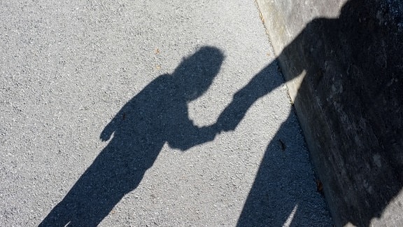 Ein Schatten zeigt ein kleines Mädchen an der Hand eines Erwachsenen.