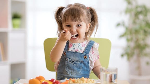 Ein kleines Mädchen isst im Kindergarten.