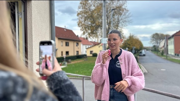 EIne junge Frau wird mit einem Smartphone gefilmt.