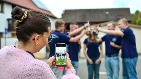 Eine Junge Frau nimmt mit dem Samtphone eine Gruppe junger Menschen auf, die mit Bierflaschen anstoßen.