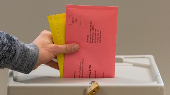 Ein Mann wirft zwei Briefumschläge mit den Stimmzetteln für die Kommunalwahlen und die Europawahlen in eine Wahlurne.