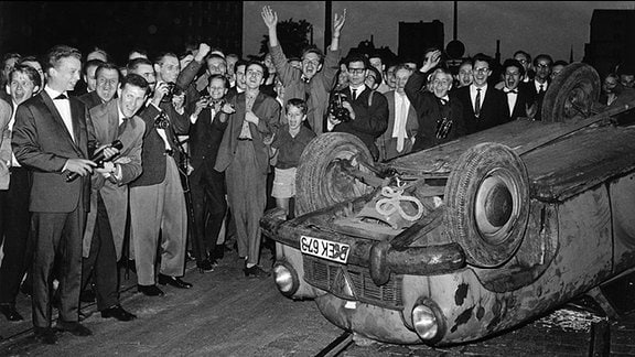 Jugendliche Demonstanten hinter einem umgestürzten Autowrack in der Kochstraße am frühen Morgen des 20.08.1962.