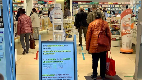 Menschenschlange in einer Apotheke - Verhaltenshinweise auf einem Schild am Eingang.