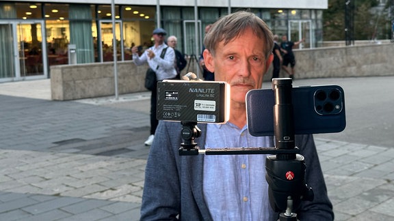 Ein Mann steht mit Aufnahmetechnik vor dem Landtagsgebäude.