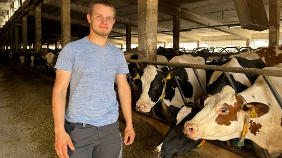 Junger Mann steht in T-Shirt einem Kuhstall