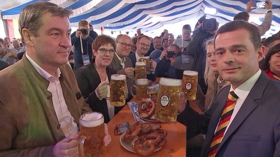 CDU-Parteichefin Annegret Kramp-Karrenbauer, CSU-Chef Markus Söder und CDU-Spitzenkandidat für die Landtagswahl 2019 Mike Mohring sitzen gemeinsam mit anderen Menschen auf Bierbänken in einem Festzelt und halten je einen Maßkrug Bier in der Hand.